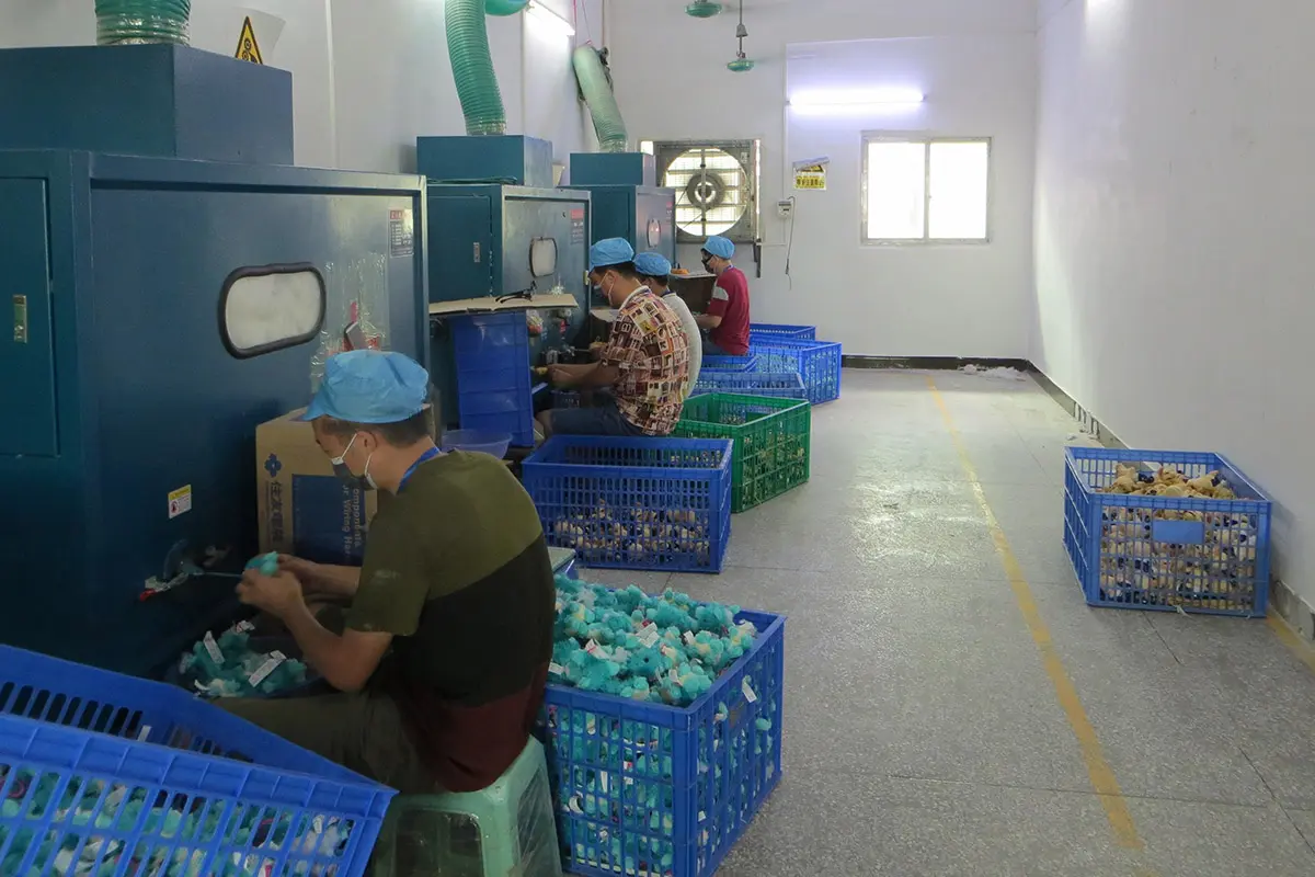 Plush toy stuffing and finishing area with workers and blue storage baskets