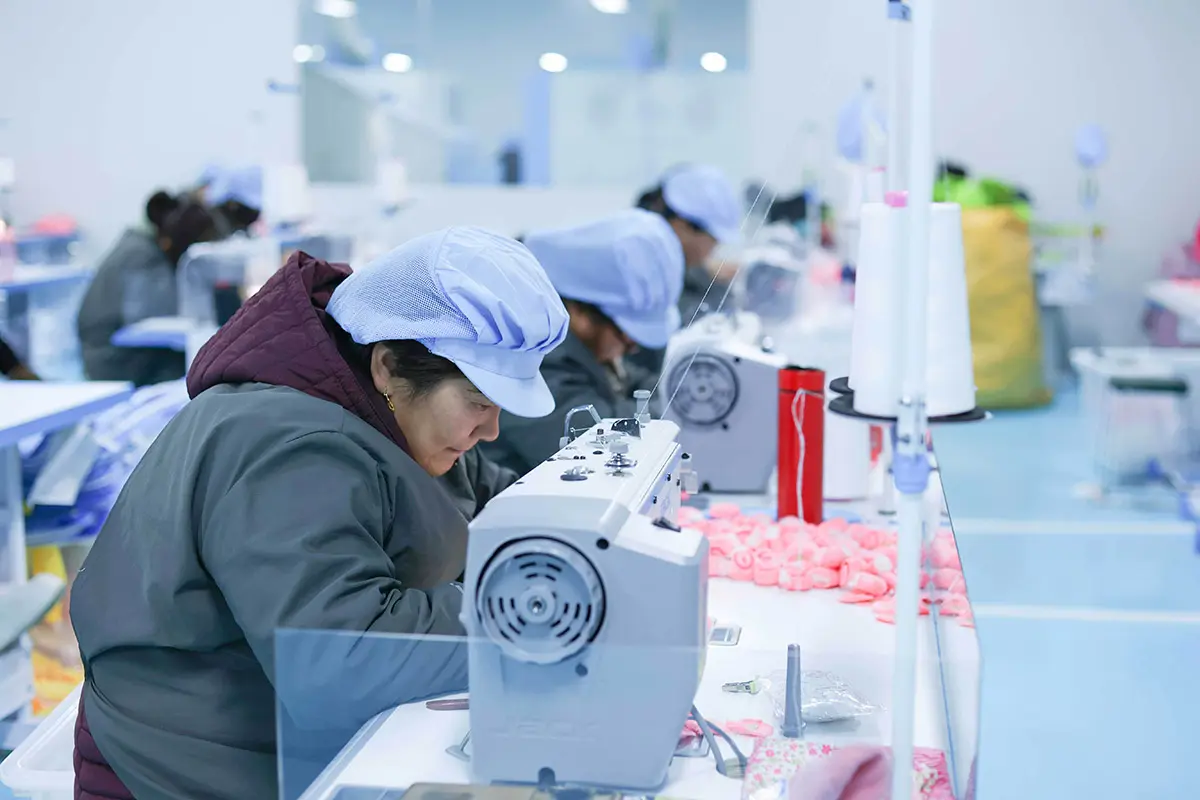 Worker sewing a custom plush sample at a factory workstation