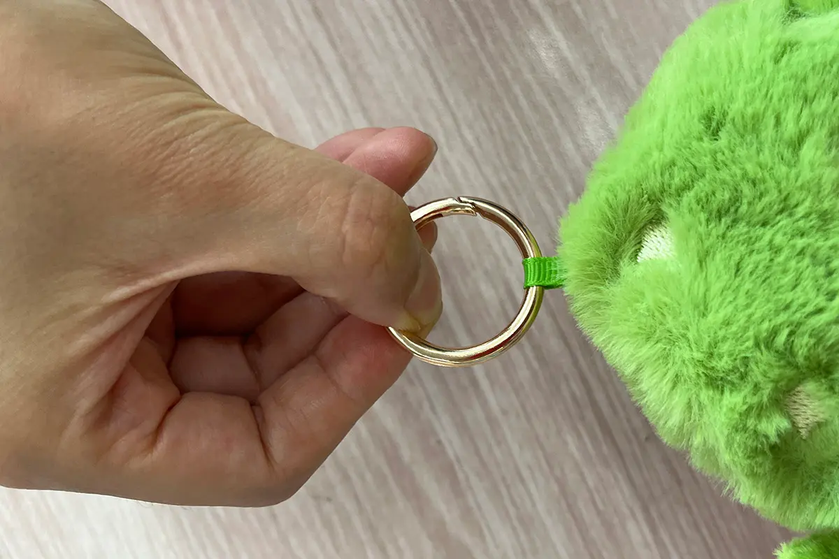 Hand pulling a metal ring on a green plush keychain to check attachment strength