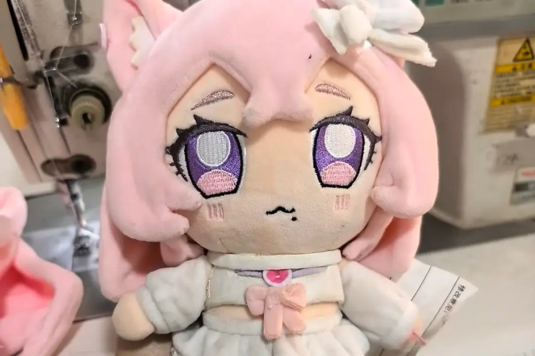Pink anime plush sample with embroidered eyes and face details during review