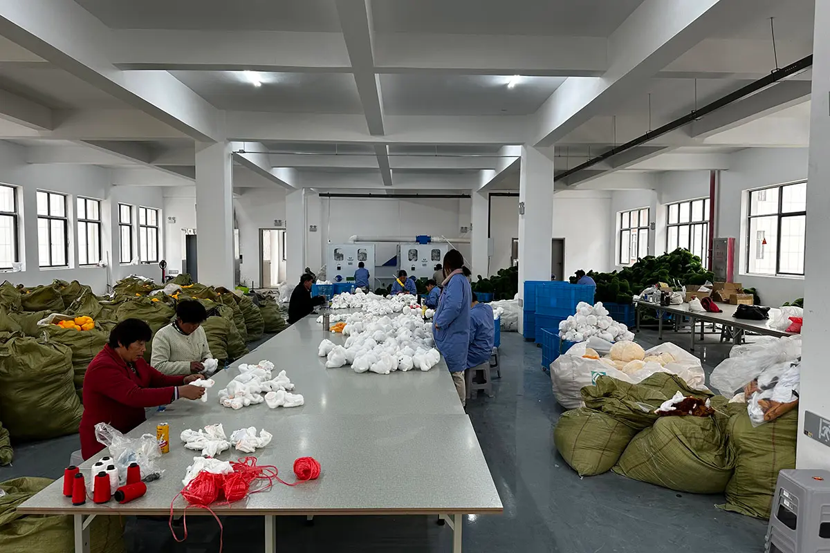Plush toy factory workers hand sewing and sorting white plush pieces at production tables